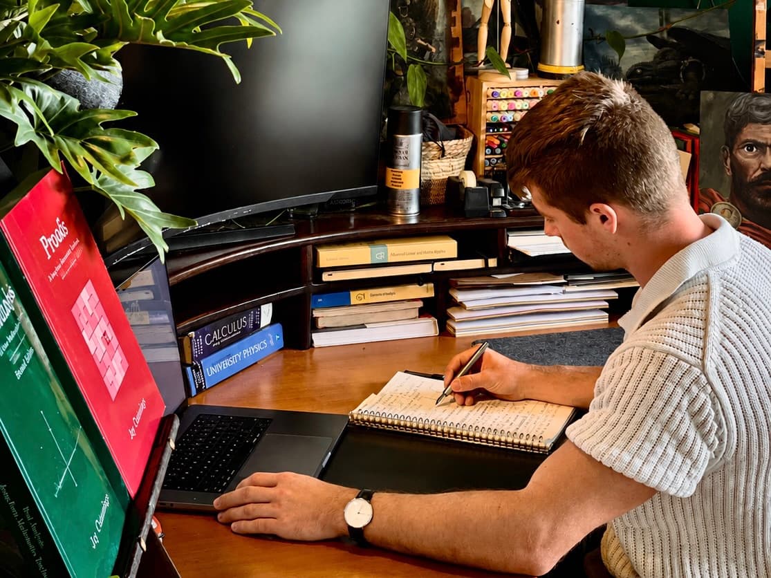 Leto writing lecture notes at his desk, beside stacked mathematics textbooks